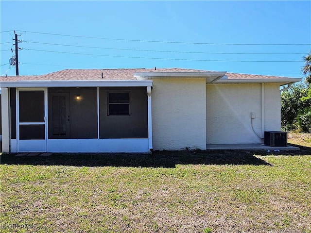 rear view of property featuring a sunroom, a yard, central AC, and stucco siding