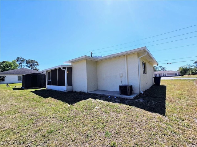 back of house with a yard, central AC unit, a sunroom, and stucco siding