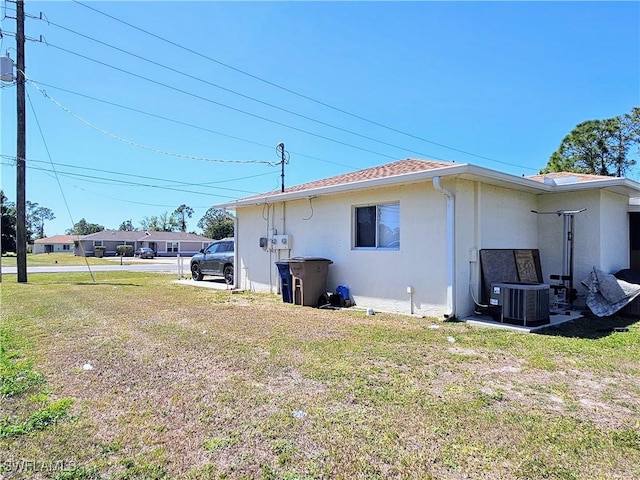 view of side of home with a yard, central AC unit, and stucco siding