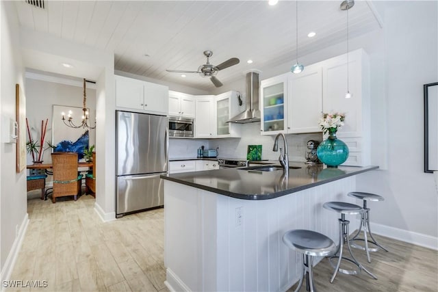 kitchen featuring wall chimney exhaust hood, a peninsula, a sink, light wood-type flooring, and appliances with stainless steel finishes