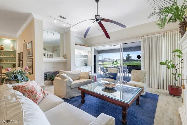 living area with a tile fireplace, wood finished floors, visible vents, ornamental molding, and ceiling fan