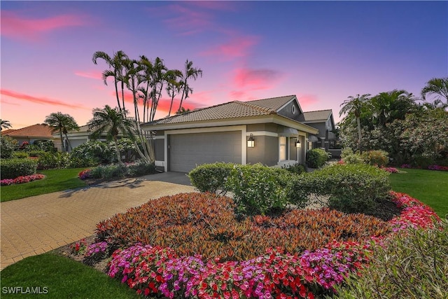 view of front of house with an attached garage, a tiled roof, driveway, and stucco siding