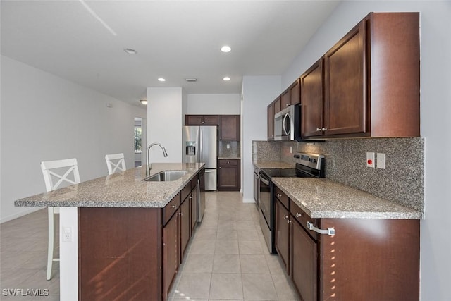 kitchen with a breakfast bar area, a center island with sink, a sink, stainless steel appliances, and backsplash