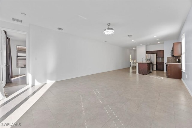 unfurnished living room with a sink, visible vents, recessed lighting, and light tile patterned floors