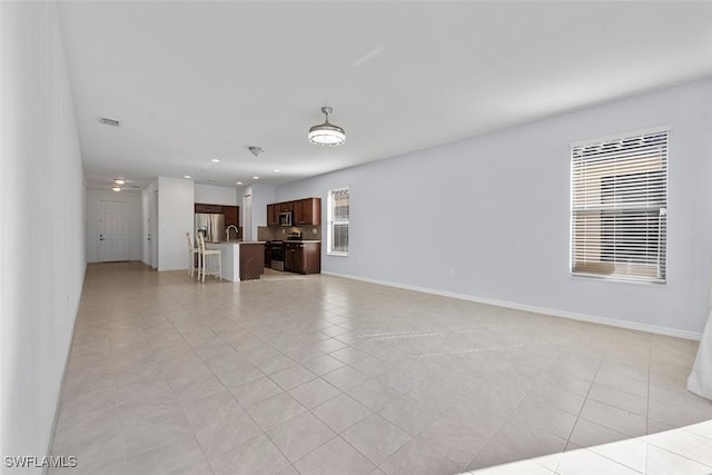 unfurnished living room featuring light tile patterned floors, visible vents, plenty of natural light, and baseboards