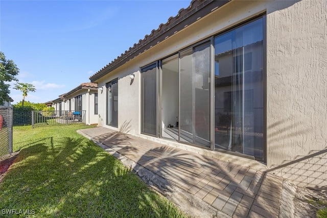 back of house with fence, stucco siding, a tiled roof, a patio area, and a lawn