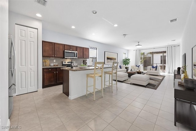 kitchen featuring visible vents, a breakfast bar, open floor plan, appliances with stainless steel finishes, and tasteful backsplash