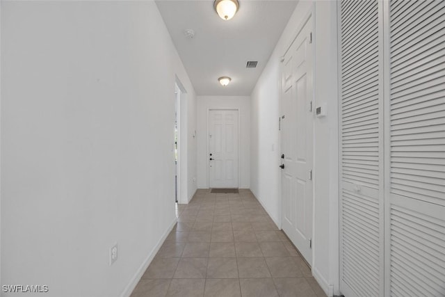 hall featuring light tile patterned flooring, visible vents, and baseboards