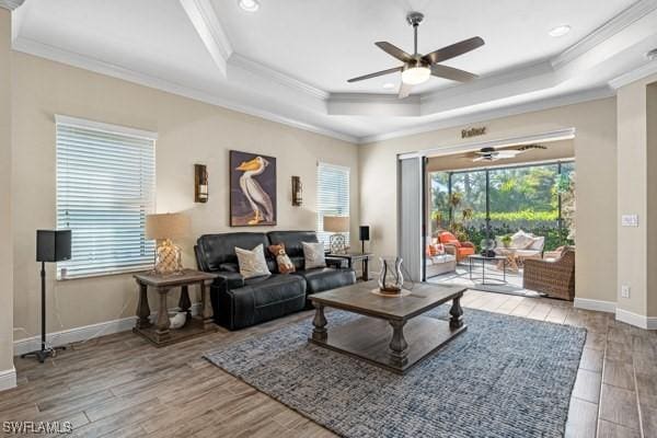 living room with wood finished floors, a ceiling fan, baseboards, ornamental molding, and a raised ceiling