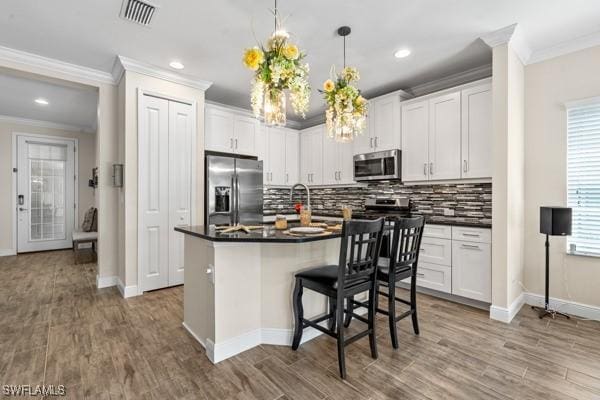 kitchen featuring dark countertops, visible vents, appliances with stainless steel finishes, and ornamental molding