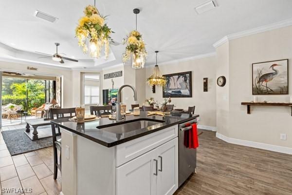 kitchen featuring dark countertops, a sink, dishwasher, crown molding, and a raised ceiling