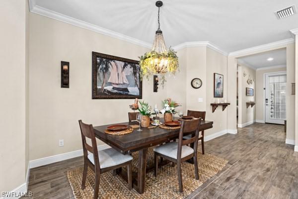 dining area featuring visible vents, crown molding, baseboards, an inviting chandelier, and wood finished floors