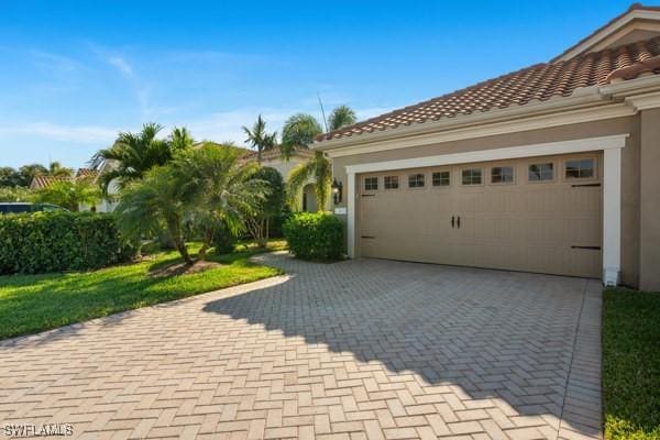 view of property exterior featuring stucco siding, decorative driveway, an attached garage, and a tile roof