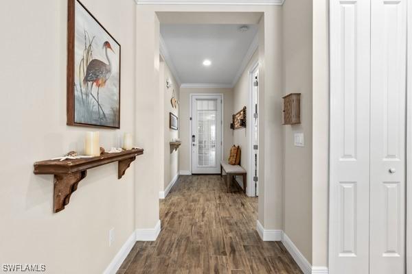 hallway with crown molding, baseboards, and dark wood-style flooring