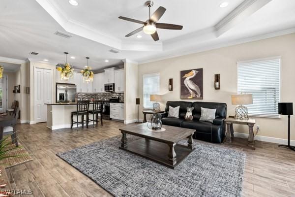 living room with a tray ceiling, wood finished floors, ceiling fan with notable chandelier, and ornamental molding