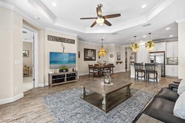 living room with crown molding, baseboards, light wood-type flooring, a raised ceiling, and a ceiling fan