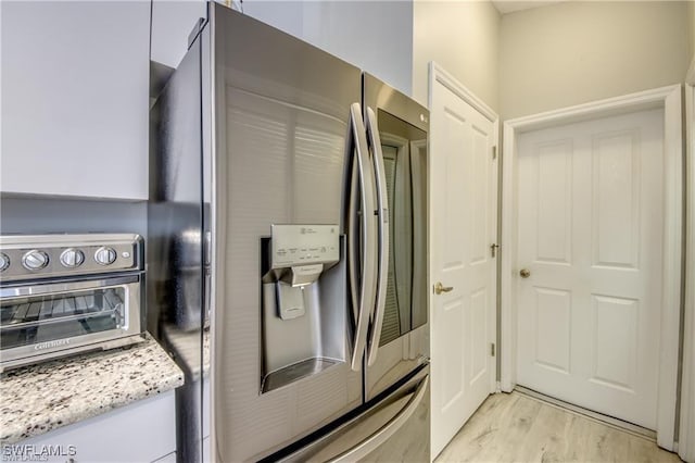 kitchen with light stone counters, light wood-style floors, stainless steel fridge with ice dispenser, and a toaster