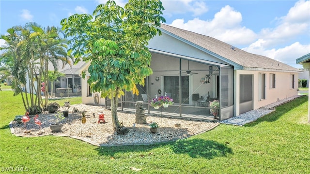 rear view of house with stucco siding, a lawn, and ceiling fan