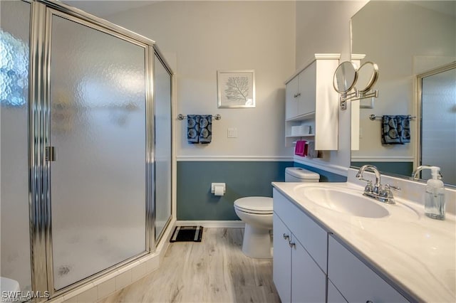 bathroom with baseboards, toilet, a stall shower, wood finished floors, and vanity