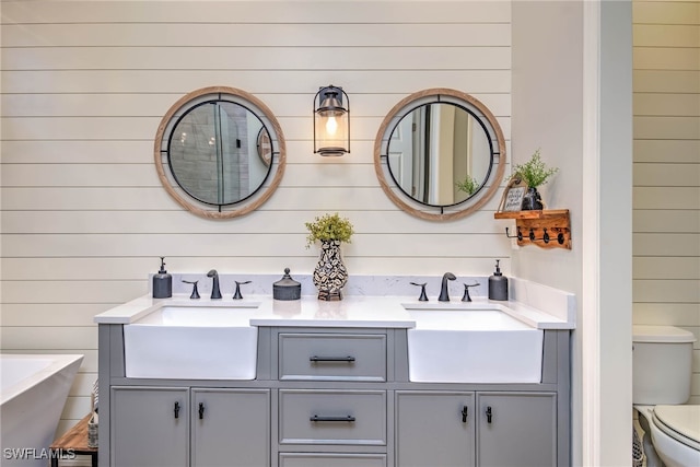 full bathroom with double vanity, a freestanding bath, toilet, and a sink