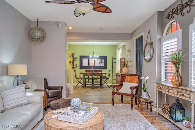 living area featuring stairway, ceiling fan with notable chandelier, baseboards, and wood finished floors