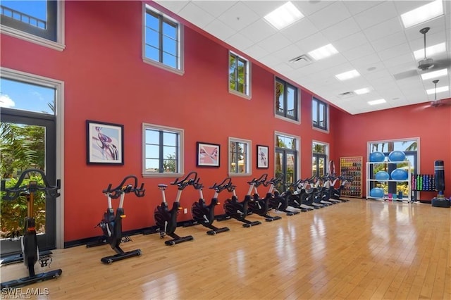 exercise room featuring a drop ceiling, a high ceiling, visible vents, and hardwood / wood-style floors