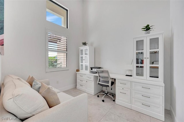 office space featuring light tile patterned flooring, built in desk, baseboards, and a towering ceiling