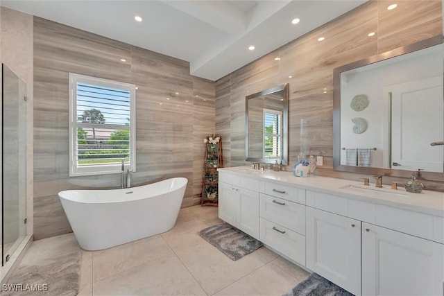 full bathroom featuring tile walls, a freestanding tub, double vanity, and a sink