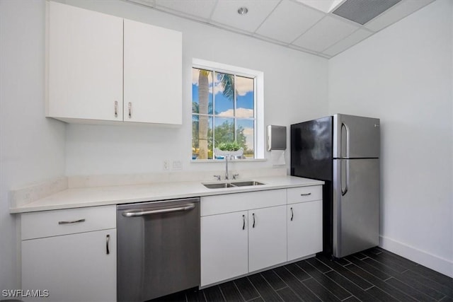 kitchen with a sink, white cabinetry, appliances with stainless steel finishes, light countertops, and a paneled ceiling