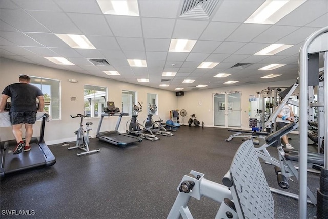 exercise room featuring visible vents, a paneled ceiling, and baseboards