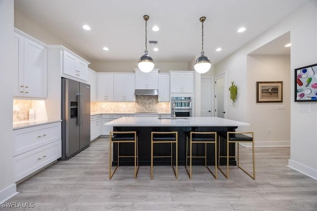 kitchen with a kitchen bar, under cabinet range hood, tasteful backsplash, appliances with stainless steel finishes, and light countertops