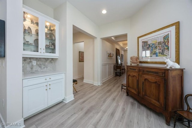 hallway with a decorative wall, recessed lighting, light wood-type flooring, and wainscoting