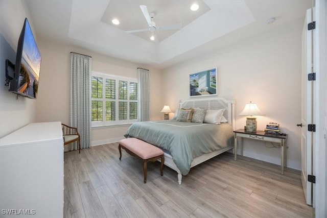 bedroom with light wood-type flooring, recessed lighting, baseboards, a raised ceiling, and ceiling fan