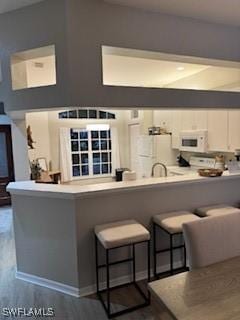 12713 Devonshire Lakes Dr, Fort Myers, FL 33913 - kitchen featuring white cabinets, a kitchen bar, dark wood-style floors, and white microwave