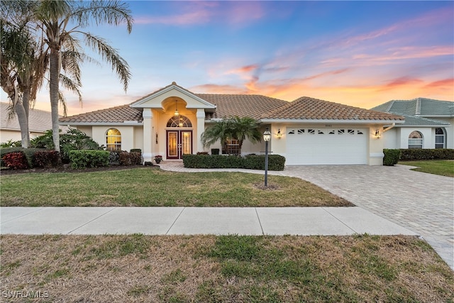 view of front of house featuring a front lawn, a tiled roof, stucco siding, decorative driveway, and a garage