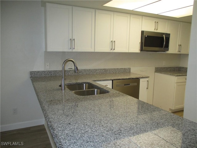 kitchen with wood finished floors, baseboards, a sink, appliances with stainless steel finishes, and white cabinetry