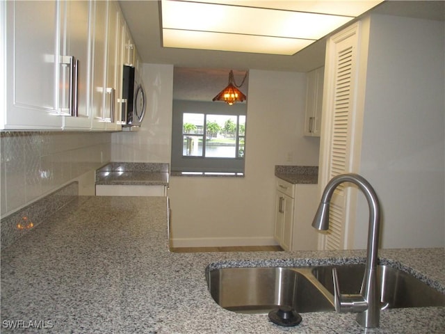 kitchen with a sink, stainless steel microwave, stone countertops, and tasteful backsplash