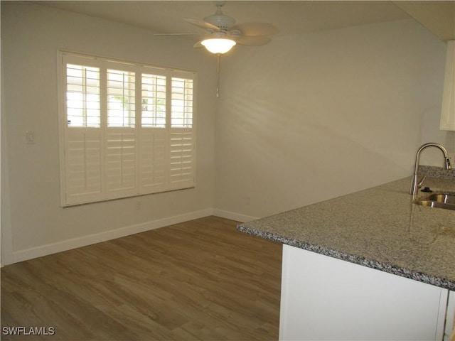 unfurnished dining area with baseboards, wood finished floors, ceiling fan, and a sink