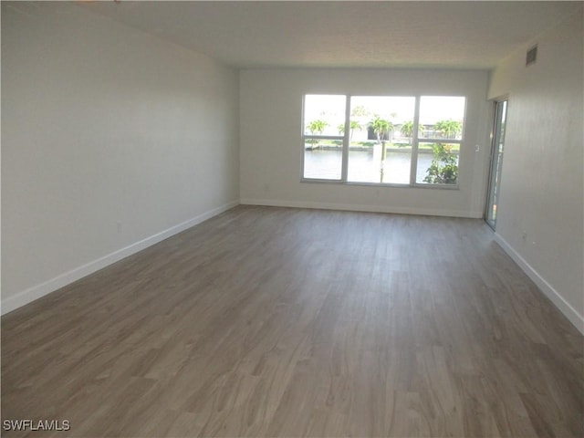 spare room with visible vents, a water view, baseboards, and wood finished floors