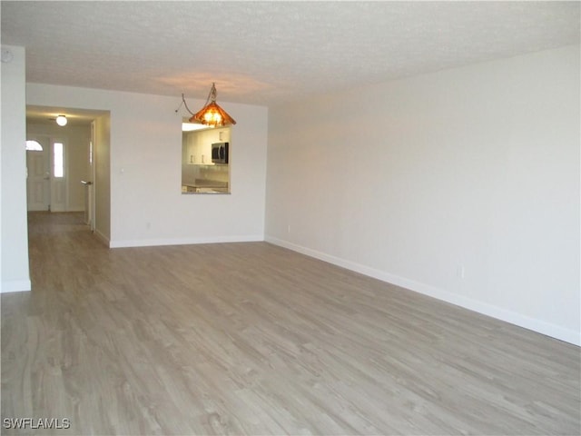 unfurnished room with light wood-style floors, baseboards, and a textured ceiling