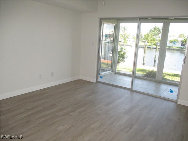 unfurnished room with baseboards, a water view, and wood finished floors