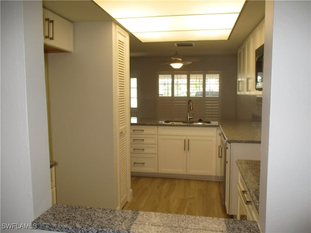 kitchen featuring a ceiling fan, light wood finished floors, stone countertops, a sink, and white cabinetry
