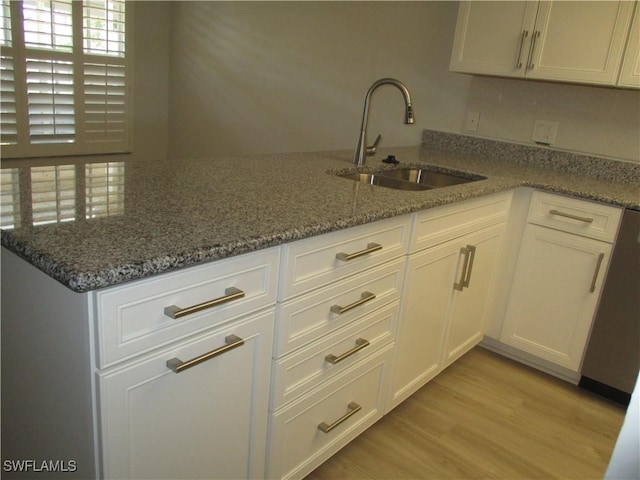 kitchen featuring stone counters, a peninsula, a sink, light wood-style floors, and white cabinetry