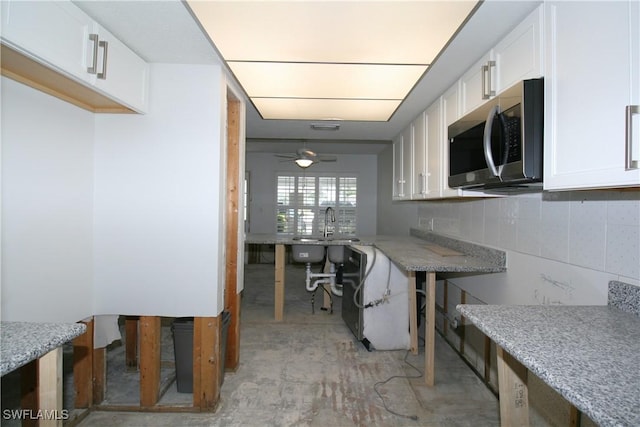 kitchen featuring stainless steel microwave, white cabinets, light stone counters, and backsplash