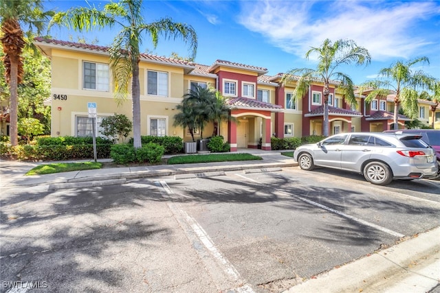 multi unit property with a tiled roof, uncovered parking, a residential view, and stucco siding