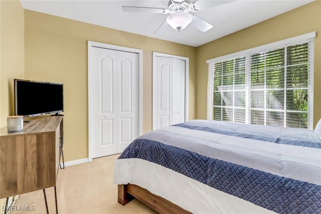 bedroom featuring ceiling fan, baseboards, multiple closets, and light carpet