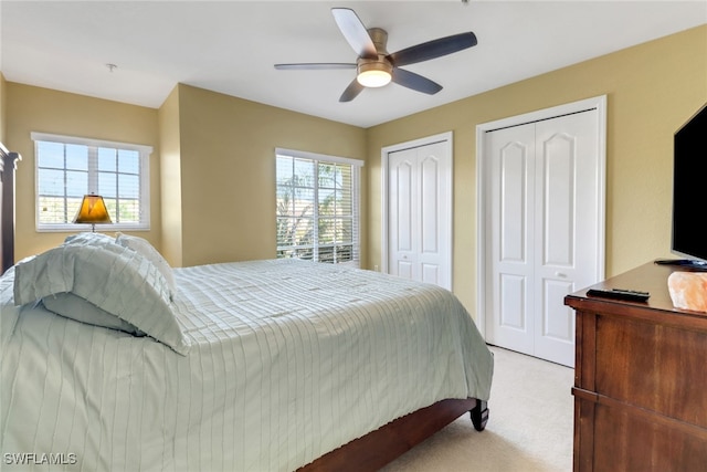 bedroom featuring light colored carpet, two closets, and ceiling fan