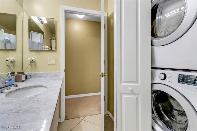 laundry room featuring light tile patterned floors, baseboards, stacked washing maching and dryer, laundry area, and a sink