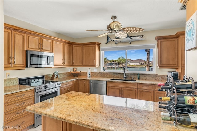 kitchen with light stone counters, brown cabinetry, ceiling fan, a sink, and appliances with stainless steel finishes