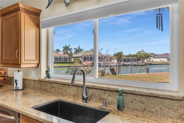 kitchen with light stone counters, a residential view, a sink, a water view, and brown cabinets